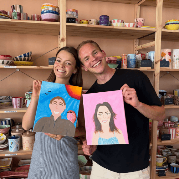 Deux personnes présentant des portraits peints dans un atelier